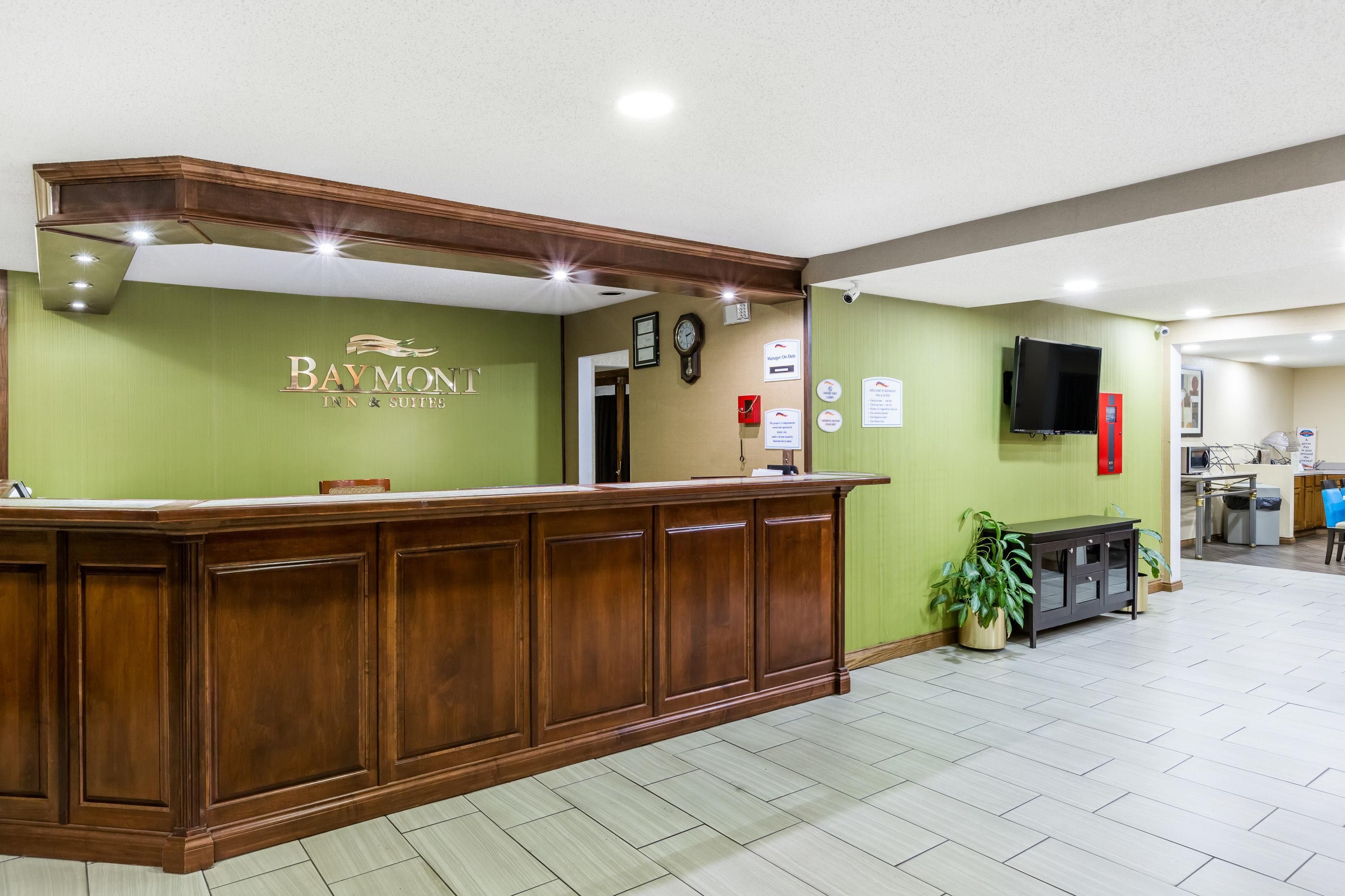 A reception desk with a sign reading 'Baymont Inn & Suites' and a clock on the wall.