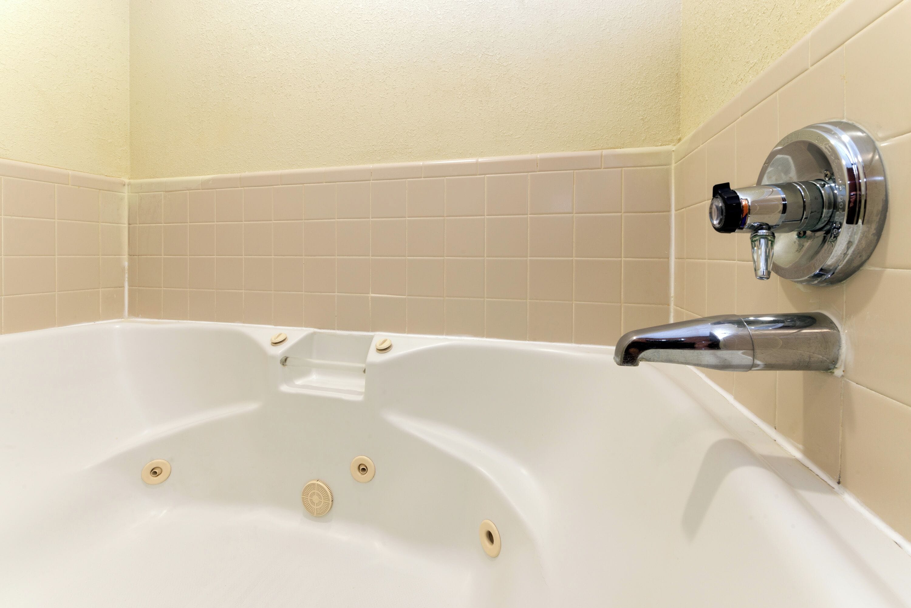 Una bañera con grifo de cromo, paredes de azulejos color beige y un diseño de azulejos en esquina.