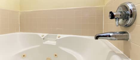 Una bañera con grifo de cromo, paredes de azulejos color beige y un diseño de azulejos en esquina.