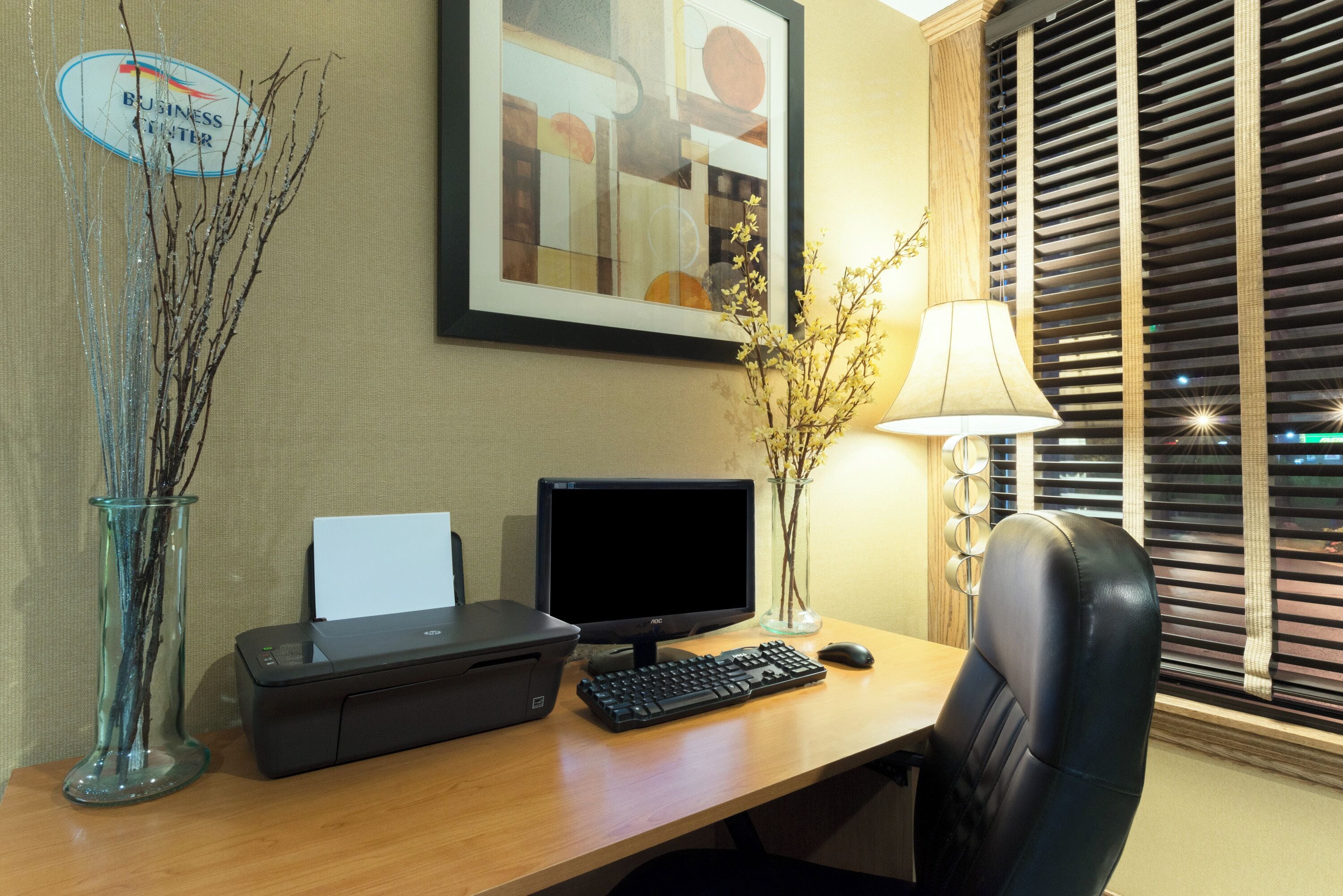 A desk with a computer, printer, and a vase with branches.