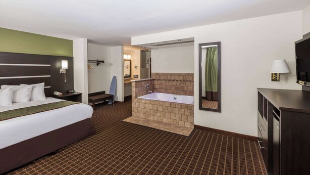 A hotel room with a large bed, a separate bathroom with a bathtub, a desk, and a mirror. - Baymont by Wyndham Louisville South/Shepherdsville/I 65 (Brooks)