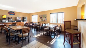 A dining area with multiple tables and chairs, a kitchen area with appliances, and a wall with a bulletin board. - Baymont by Wyndham Louisville South/Shepherdsville/I 65 (Brooks)