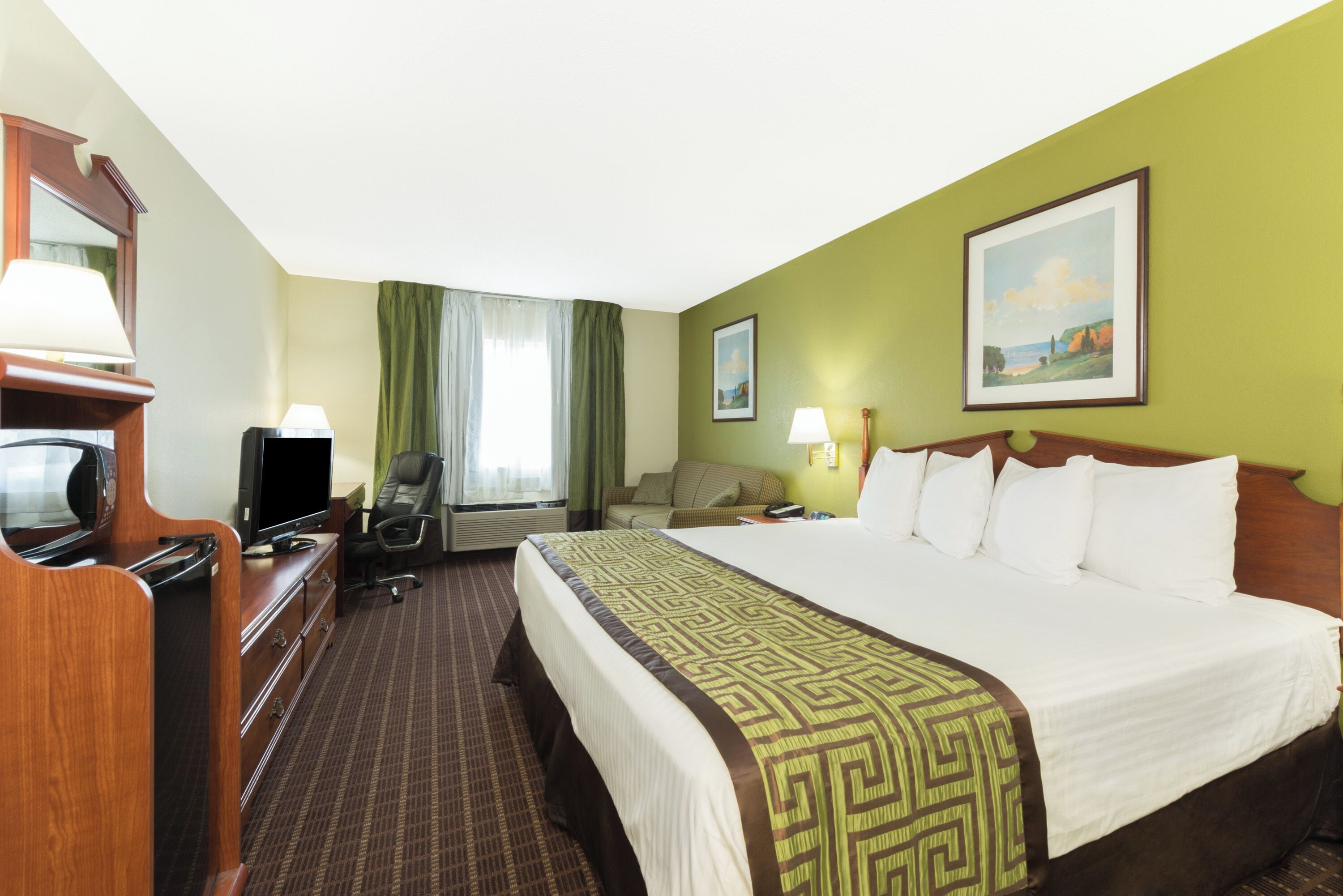 Habitación de hotel con cama, escritorio con televisor, silla, lámpara de escritorio y ventana con cortinas.