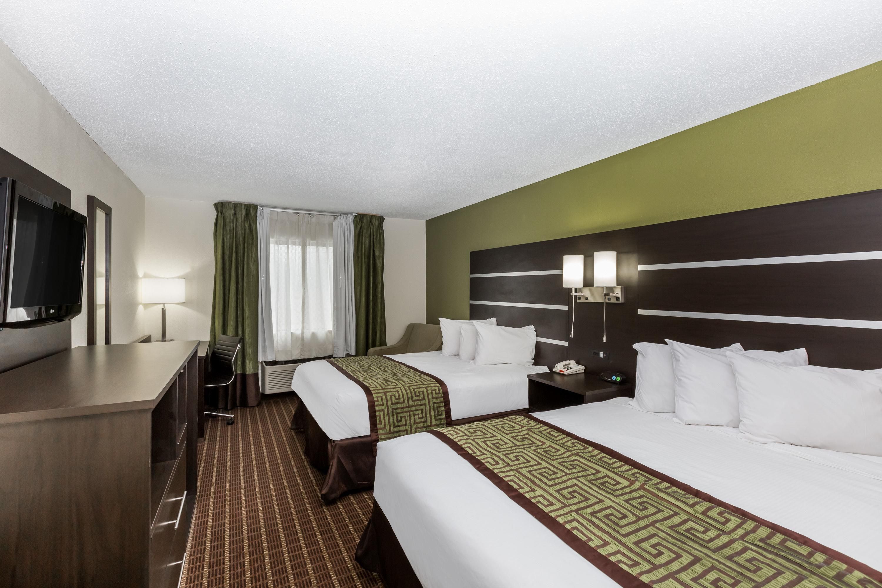 A hotel room with two beds, a desk, a television, and a window with curtains.