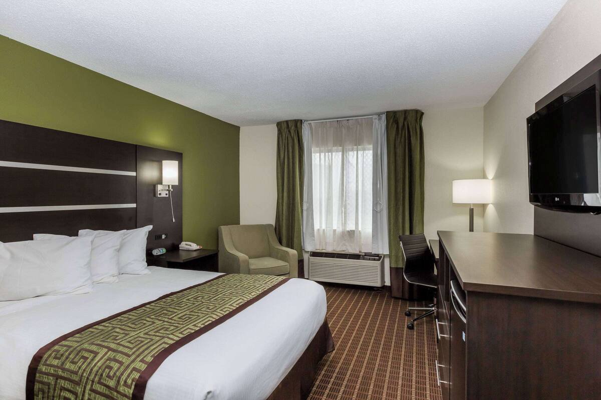Une chambre d’hôtel avec un grand lit, un bureau, une chaise, un téléviseur à écran plat et une fenêtre avec des rideaux.