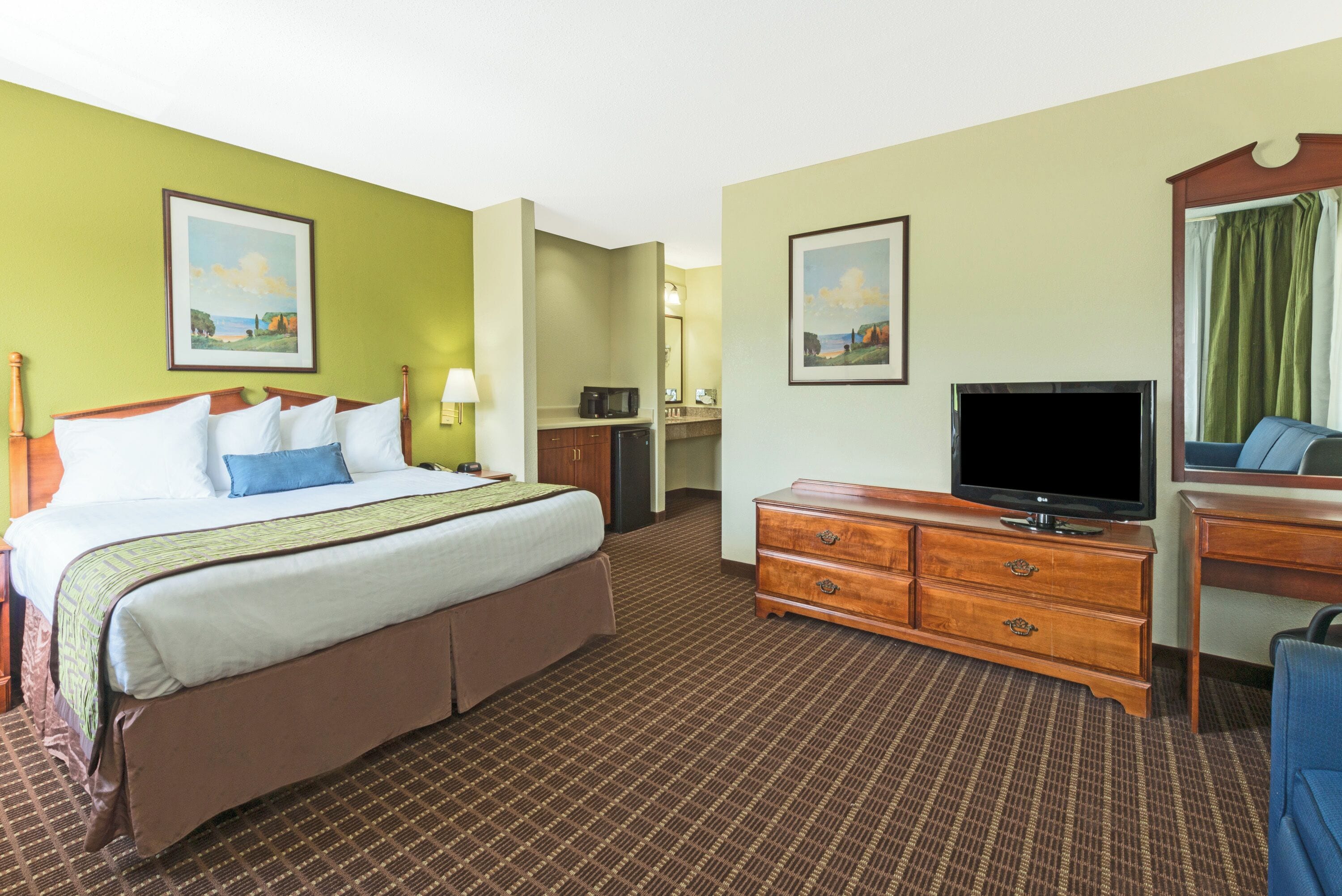 A hotel room with a bed, a television, a dresser, a desk, and a chair.
