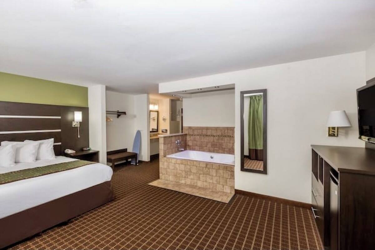 Une chambre d’hôtel avec un grand lit, une salle de bain séparée avec une baignoire, un bureau et une chaise.