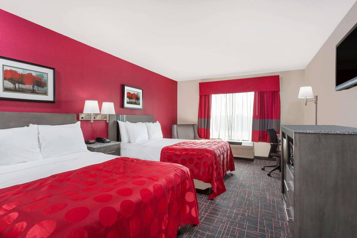 A hotel room with two beds, a desk, a chair, a television, and a window with curtains.