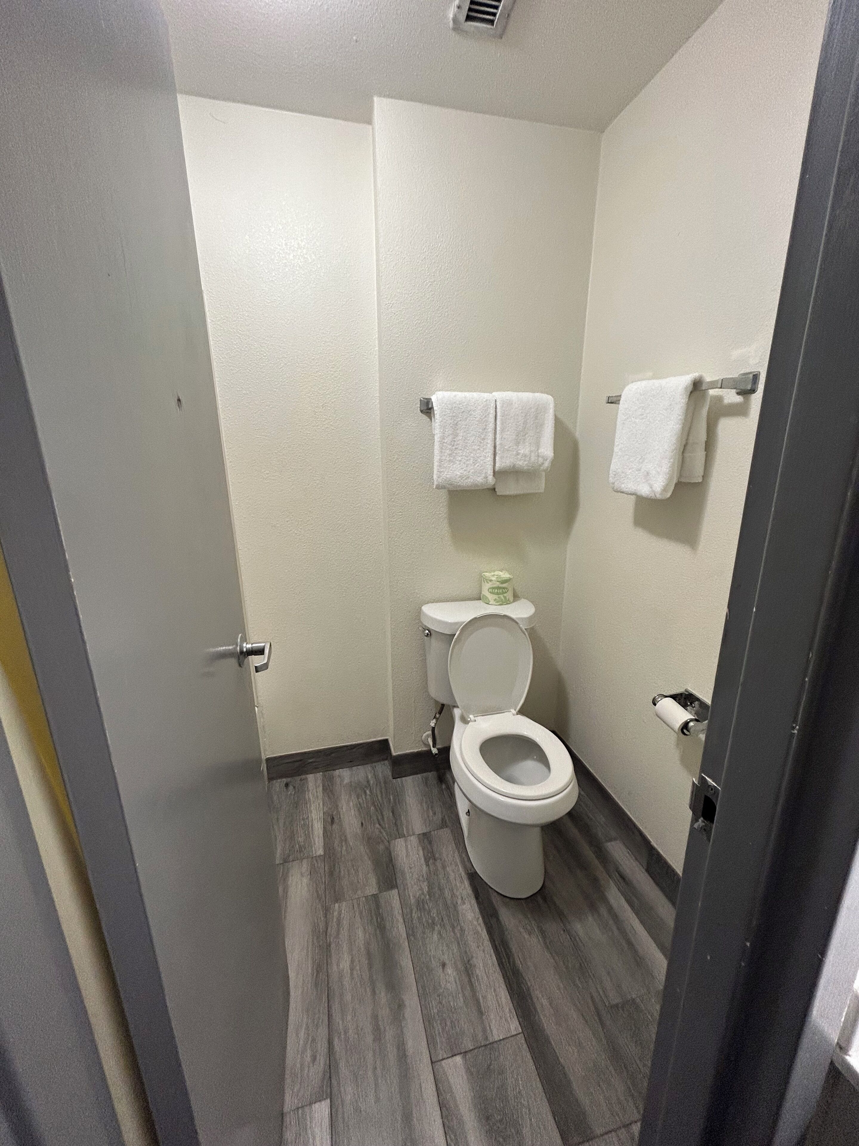 Une petite salle de bain compacte, équipée de toilettes, de deux porte-serviettes et d’un support à papier toilette.