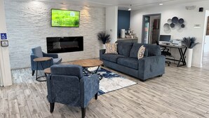 A modern living room with a flat-screen TV mounted on a textured wall, a grey sofa, a coffee table, and a blue armchair.