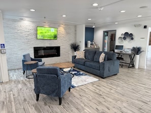 A modern living room with a flat-screen TV mounted on a textured wall, a grey sofa, a coffee table, and a blue armchair.