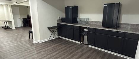 A modern kitchen with dark wood flooring, black cabinets, and stainless steel appliances.
