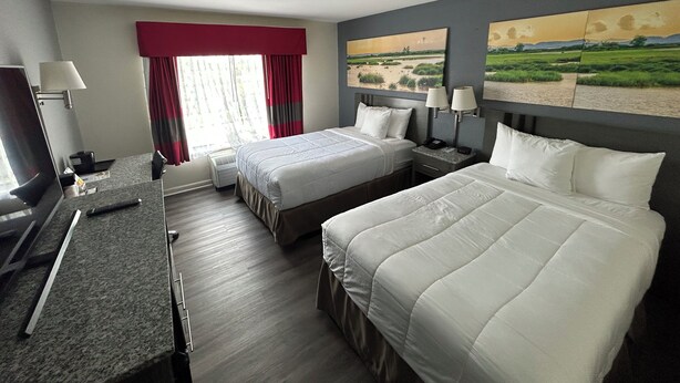 A hotel room with two beds, a desk, a TV, and a painting of a landscape. - Clarion Pointe - Greensboro Coliseum Area (Greensboro)