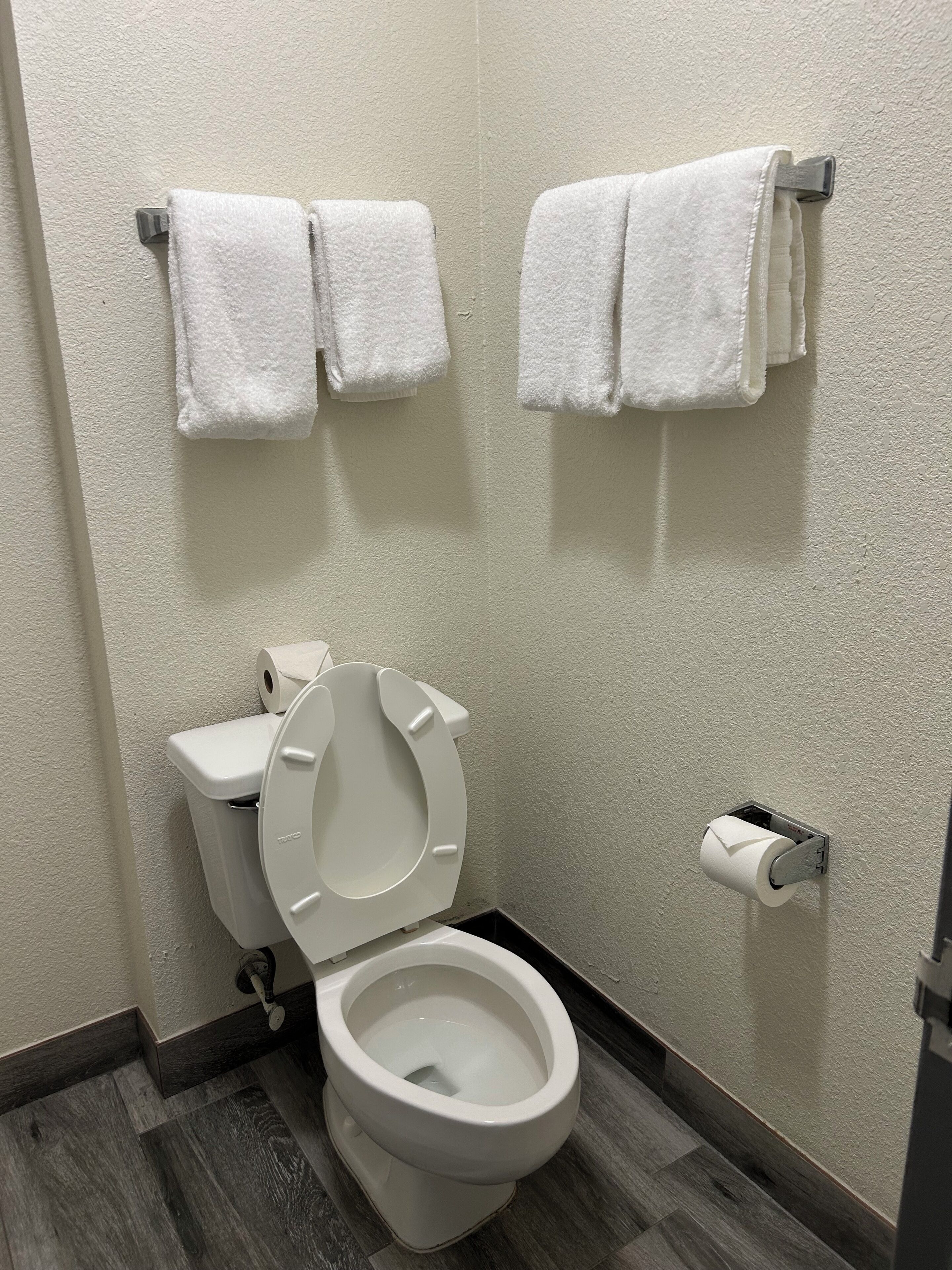 Un baño con inodoro, dispensador de toallas de papel y dos toallas colgadas en un perchero.