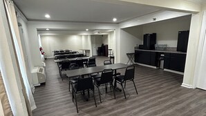 A spacious living area with a dining table and chairs, a kitchen with appliances, and a visible fire extinguisher. - Clarion Pointe - Greensboro Coliseum Area (Greensboro)