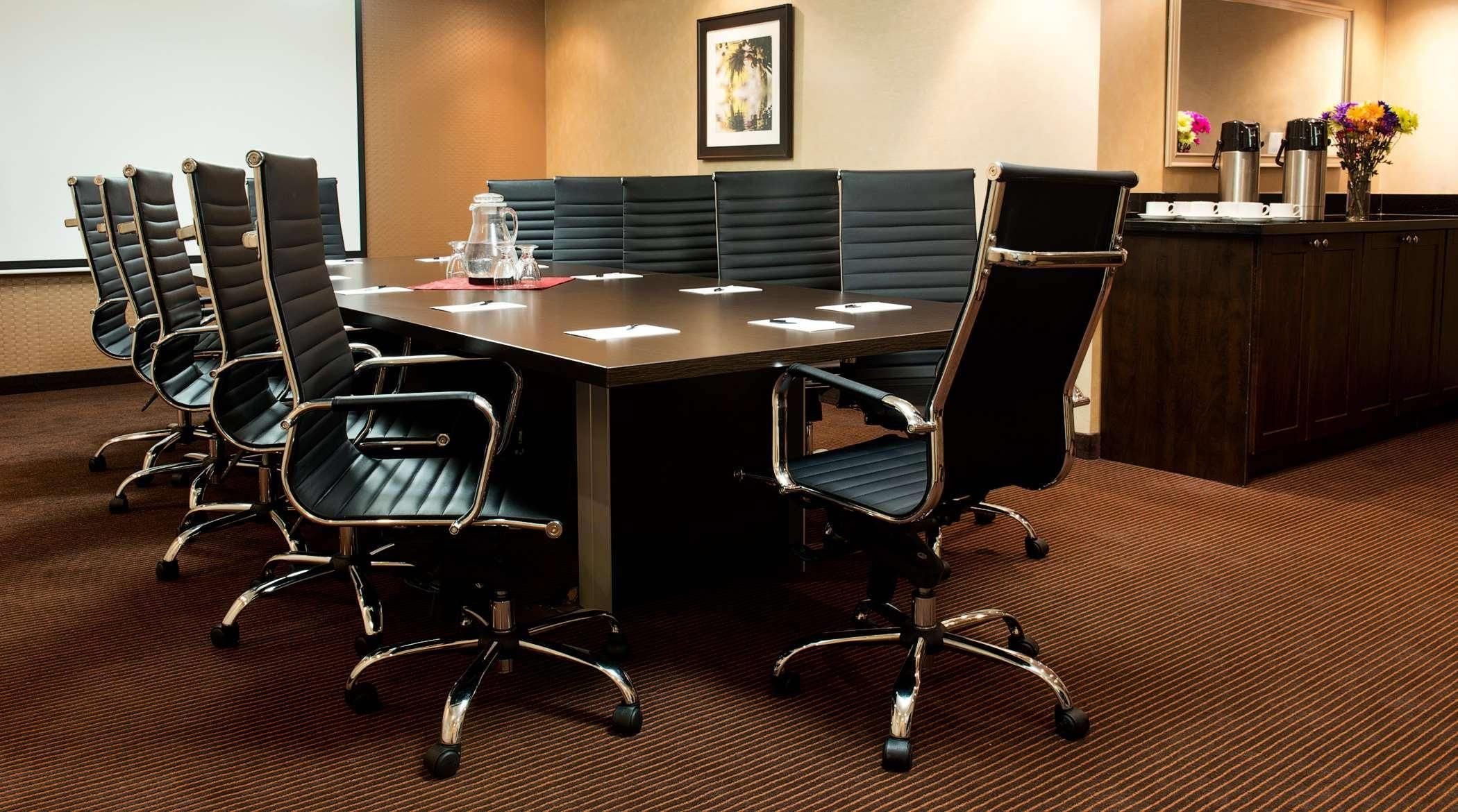 A conference room with a long table, black leather chairs, a coffee station, and a framed picture on the wall.