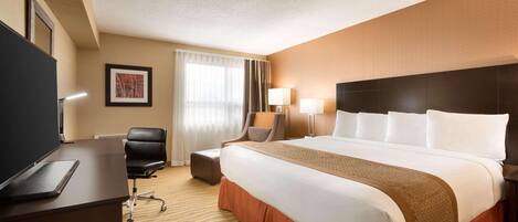 Habitación de hotel con una cama grande, un escritorio con una computadora portátil, una silla, un televisor y una ventana con cortinas.