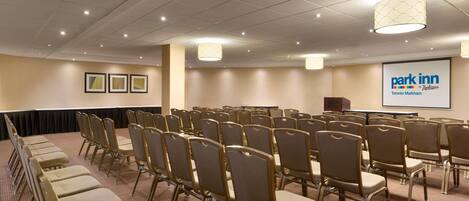 A conference room with rows of chairs, a podium, and a screen displaying 'Park Inn Toronto Markham'.