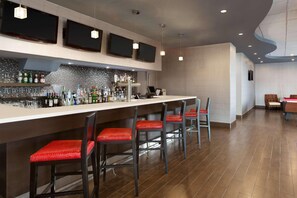 A bar area with a long counter, multiple stools, and a variety of bottles and glasses. - Park Inn By Radisson Toronto - Markham (Markham)