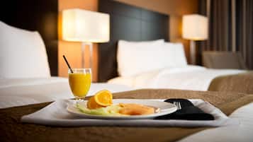 Una cama bien hecha con sábanas blancas, un plato de fruta y un vaso de zumo de naranja sobre un camino de mesa blanco.