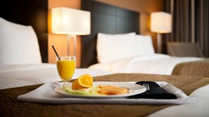 A neatly made bed with white linens, a plate of fruit and a glass of orange juice on a white placemat.