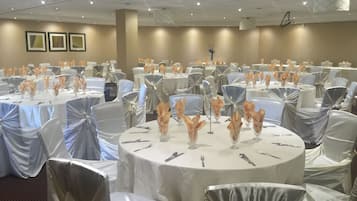 A banquet hall with round tables covered in white tablecloths, silver chair covers, and centerpieces with orange flowers.
