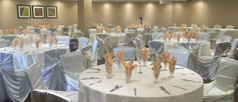 A banquet hall with round tables covered in white tablecloths, silver chair covers, and centerpieces with orange flowers.