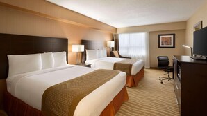 A hotel room with two beds, a desk, a chair, and a television.