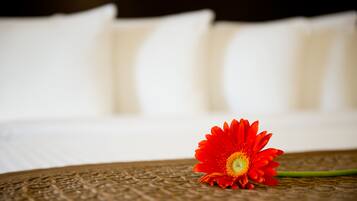 A single red flower on a textured surface with a blurred background of a bed with white pillows.