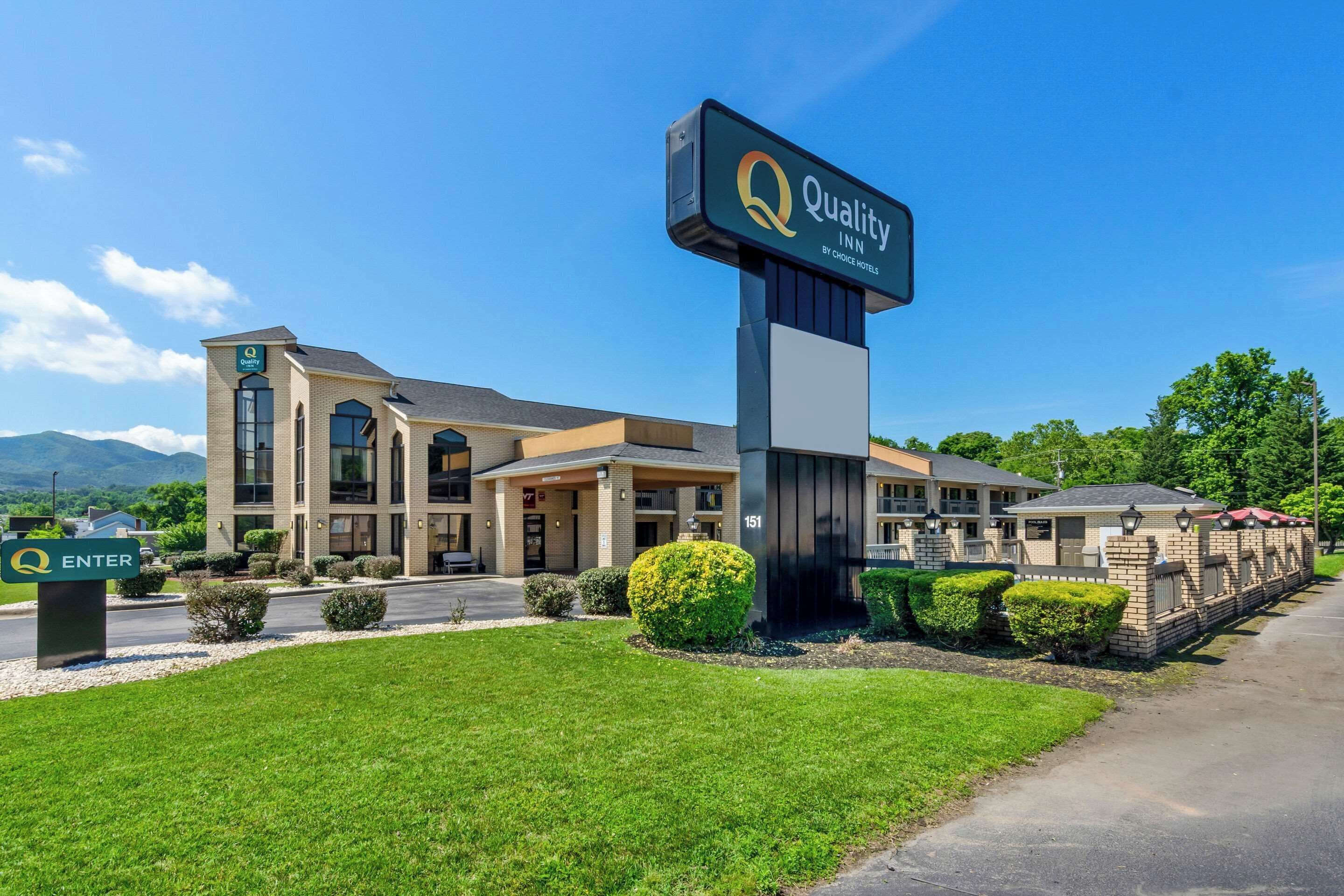 A hotel entrance with a large sign reading "Quality Inn by Choice Hotels," a well-maintained lawn, and a clear sky.