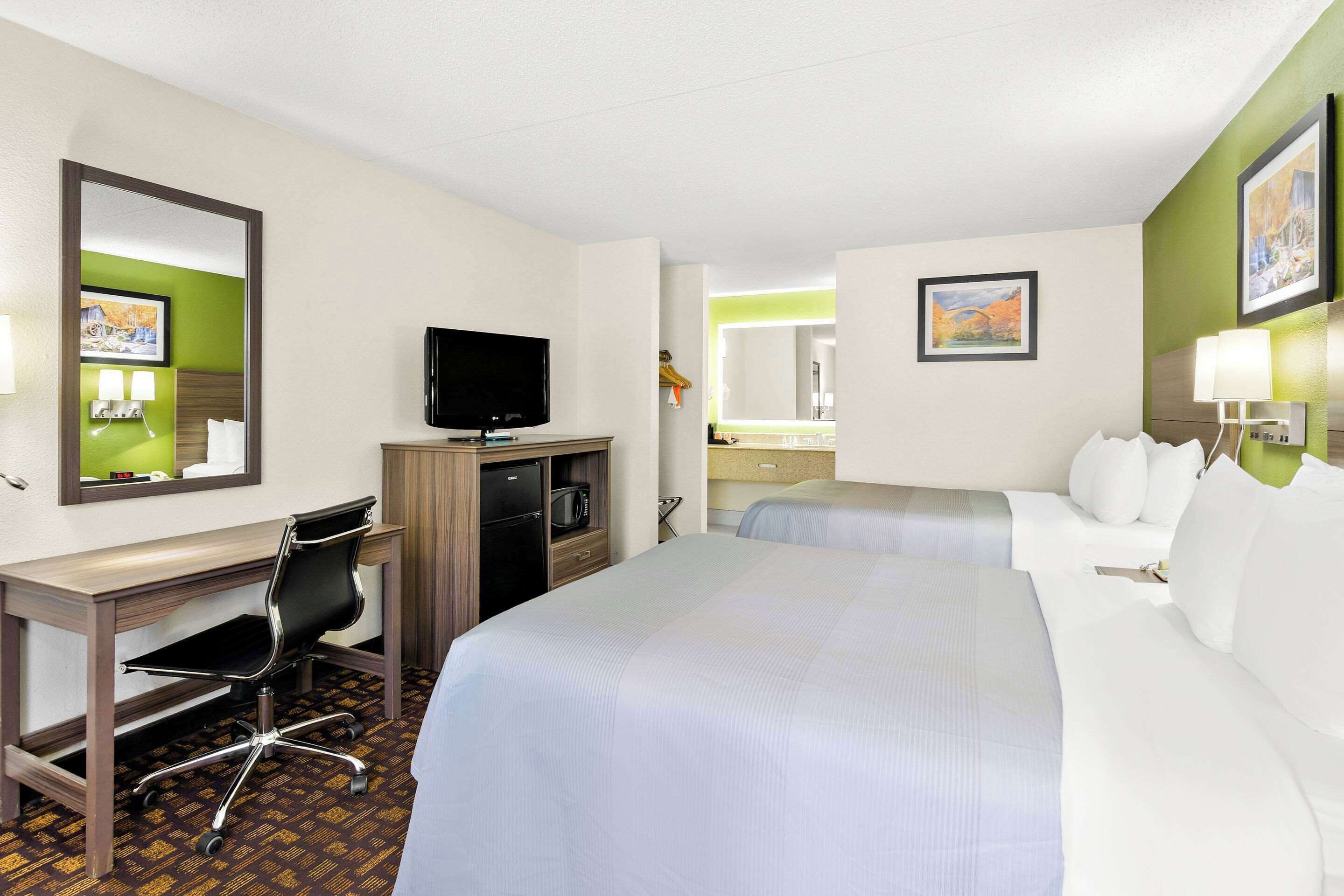 A hotel room with a bed, a desk, a chair, a television, a microwave, and a bathroom mirror.