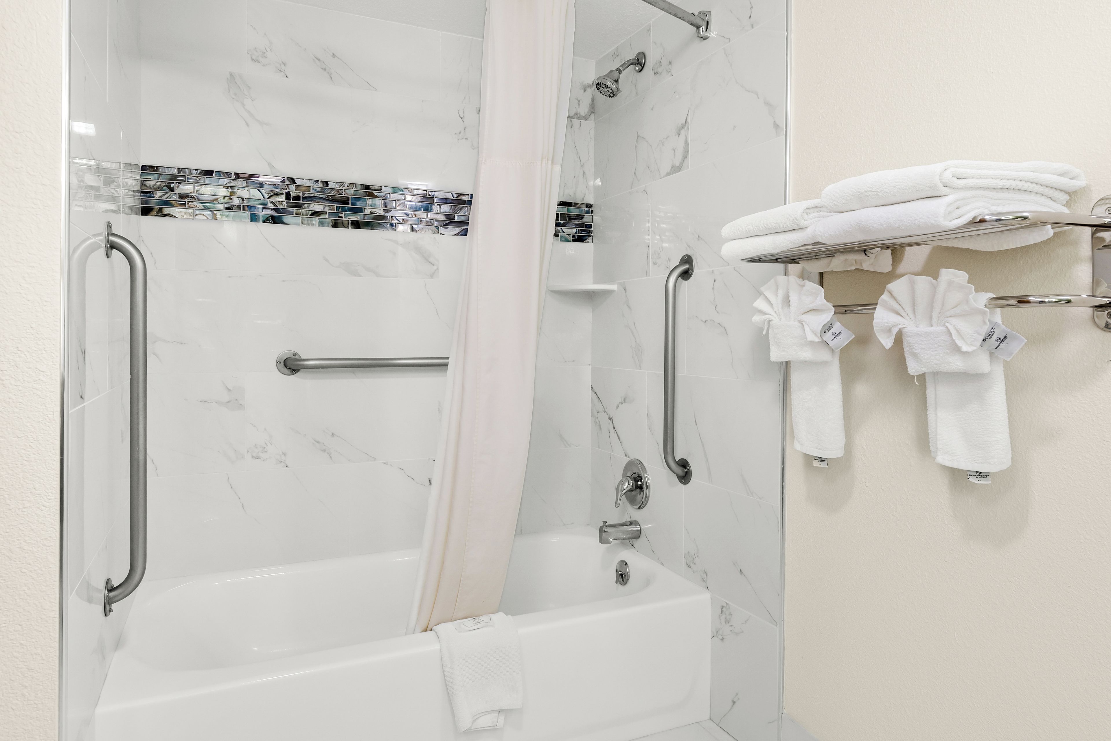 A bathroom with a bathtub, a shower with a handheld showerhead, and a towel rack with towels.