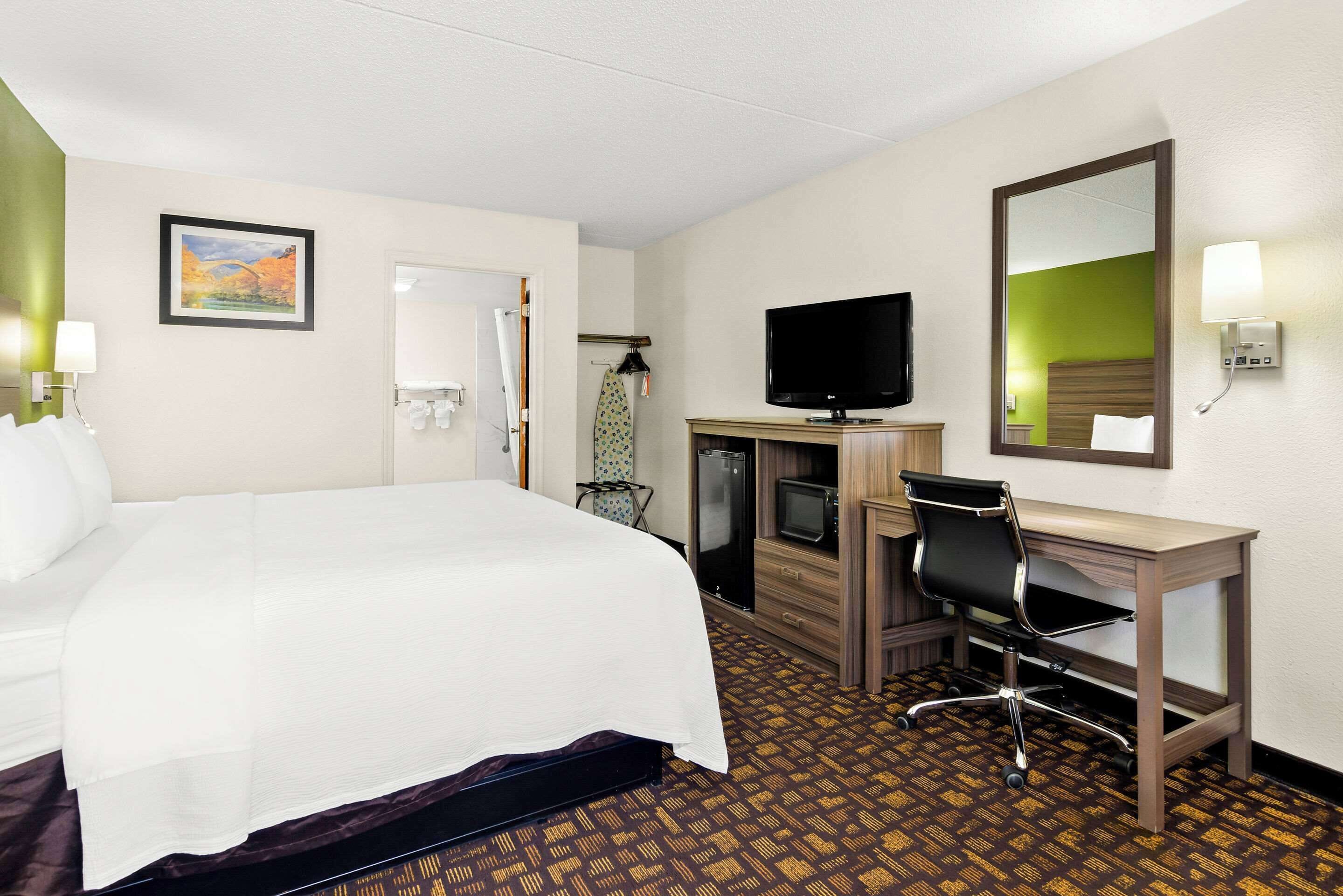 A hotel room with a large bed, a desk with a chair, a television, and a mirror.