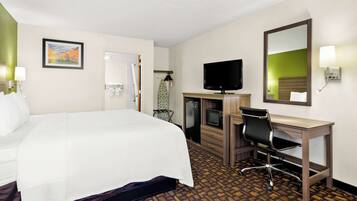A hotel room with a large bed, a desk with a chair, a television, and a mirror.