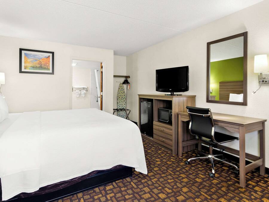 A hotel room with a large bed, a desk with a chair, a television, and a mirror.