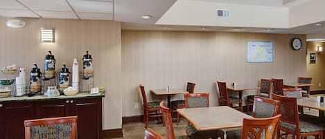 A hotel dining area with wooden tables and chairs, a coffee station, and a clock on the wall.