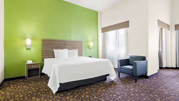 A hotel room with a large bed, a chair, a nightstand, and a green wall.