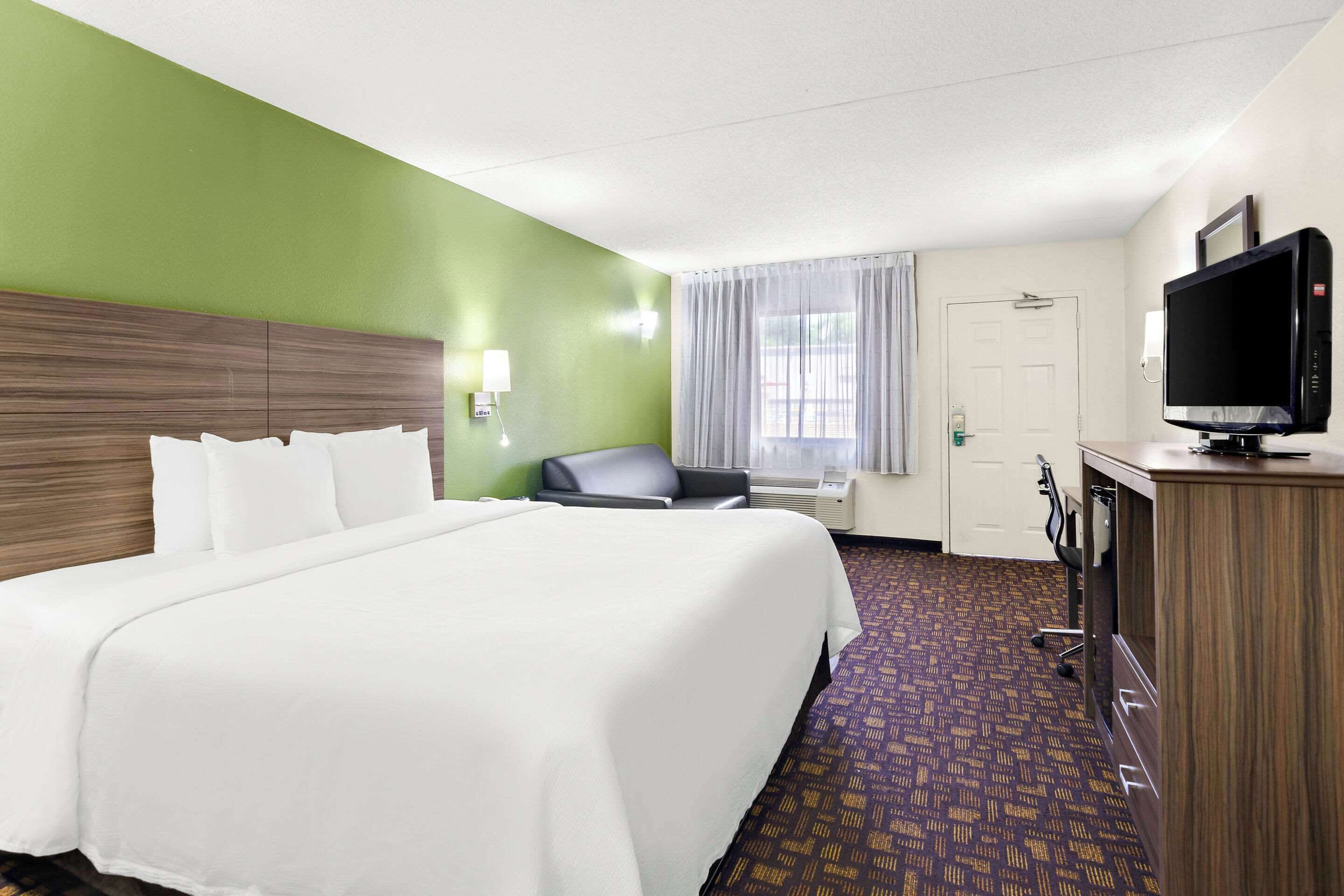 Een hotelkamer met een groot bed, een bureau met een televisie, een stoel en een bureaulamp.