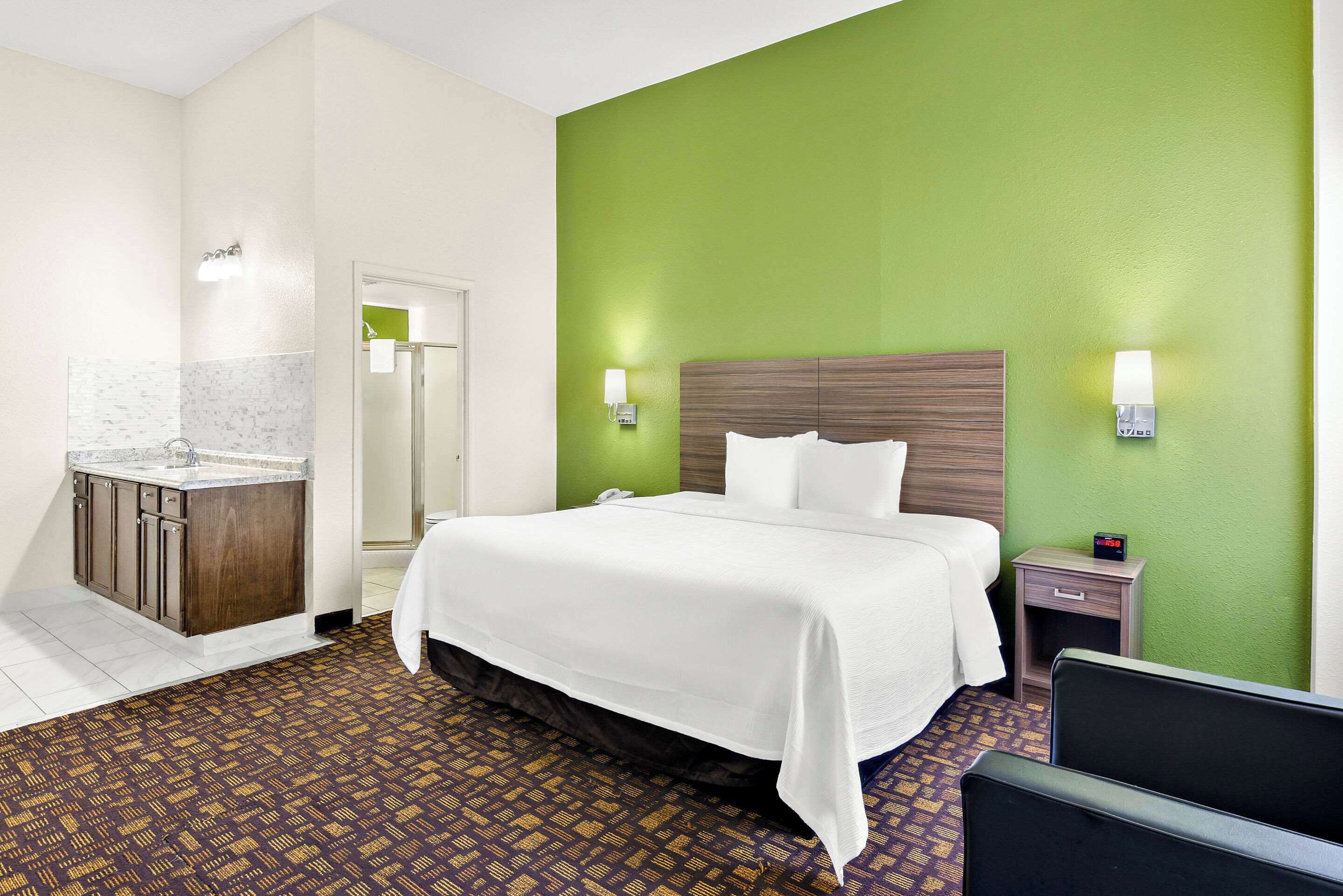 A hotel room with a bed, a nightstand, a small table, a sink, and a mirror.