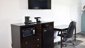 Espacio de oficina compacto con escritorio, silla, microondas, refrigerador y televisor de pantalla plana montado en la pared.