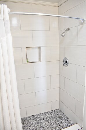 A shower with white tiles, a showerhead, and a small mirror.