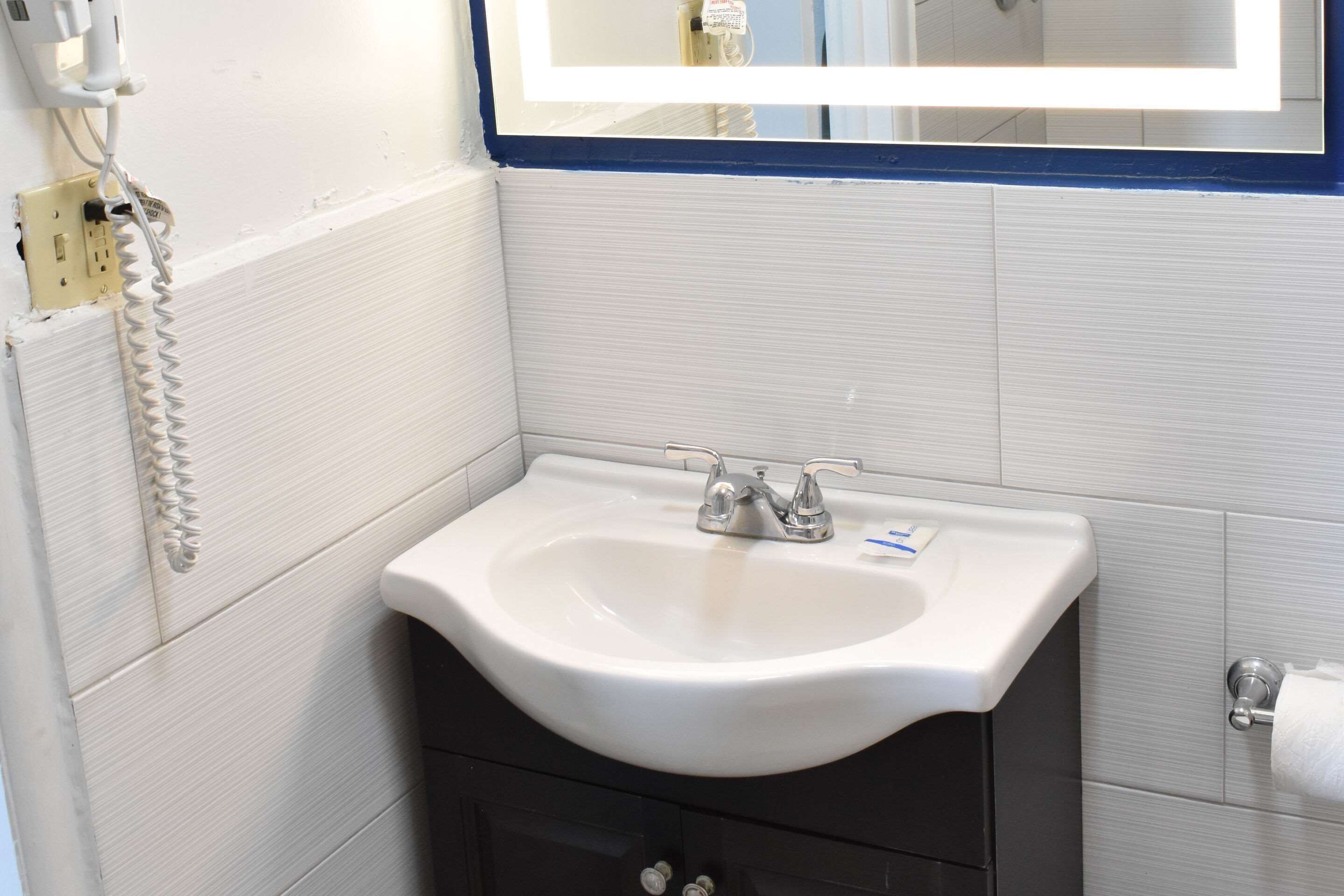Un baño con un lavamanos blanco, un espejo encima y un perchero a la derecha.