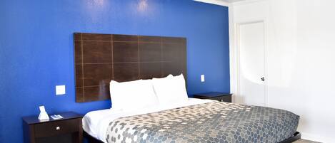 Habitación de hotel con una pared azul de acento, una cama grande con cubrecama estampado, cabecero oscuro y una mesita de noche con un teléfono y una pequeña mesa.