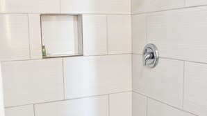 Un baño con paredes de azulejos blancos y zona de ducha.