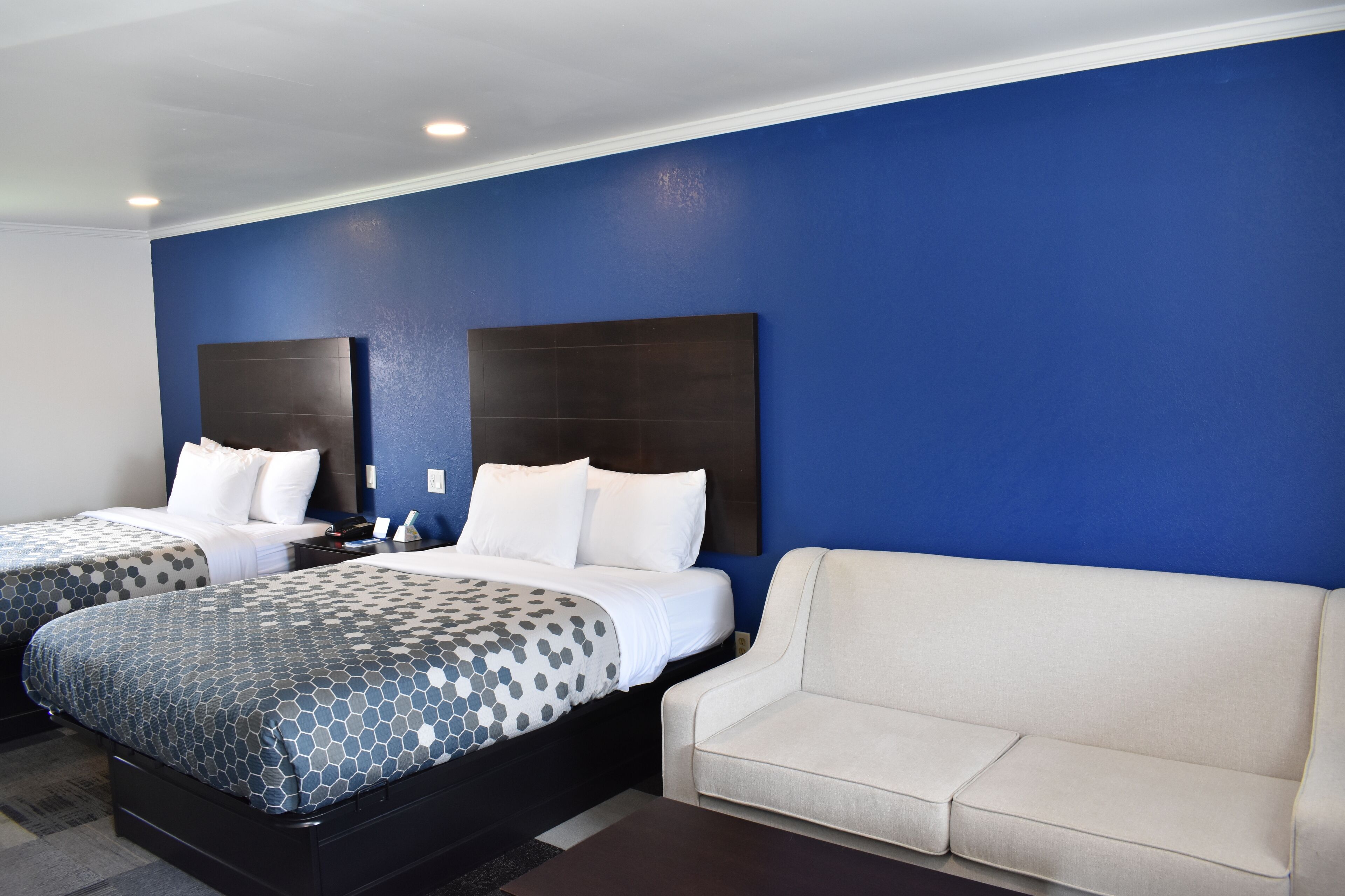 Habitación de hotel con dos camas, un sofá y un cabecero oscuro.