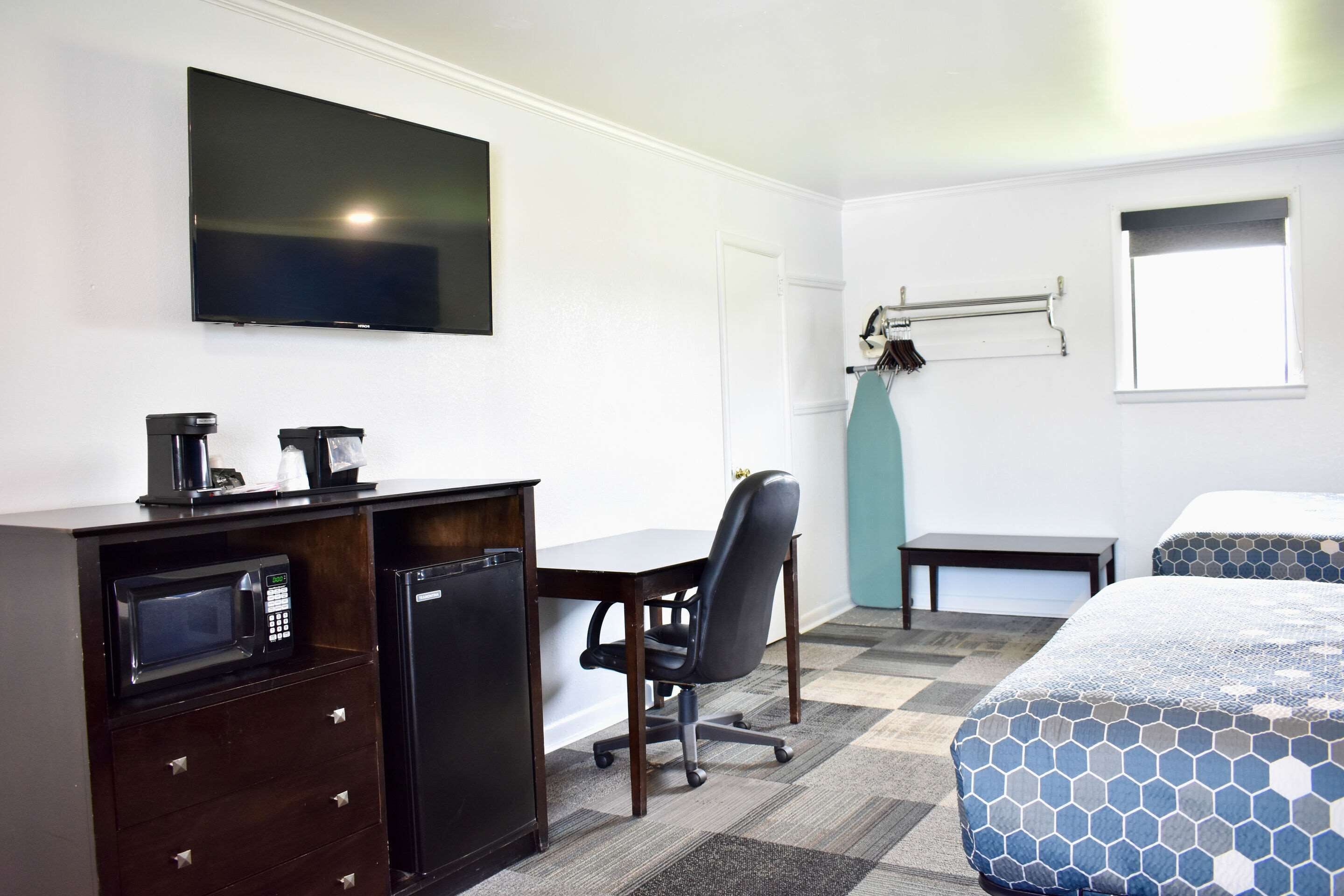 A hotel room with a bed, a desk with a microwave, a chair, a television, and a window.