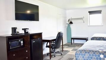 A hotel room with a bed, a desk with a microwave, a chair, a television, and a window.