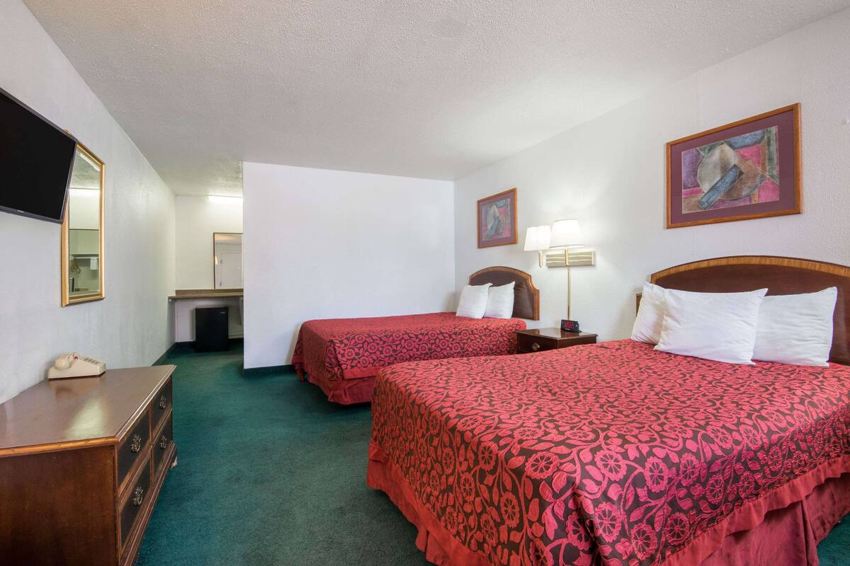 Habitación de hotel con dos camas, un aparador, un escritorio, una silla y un televisor.