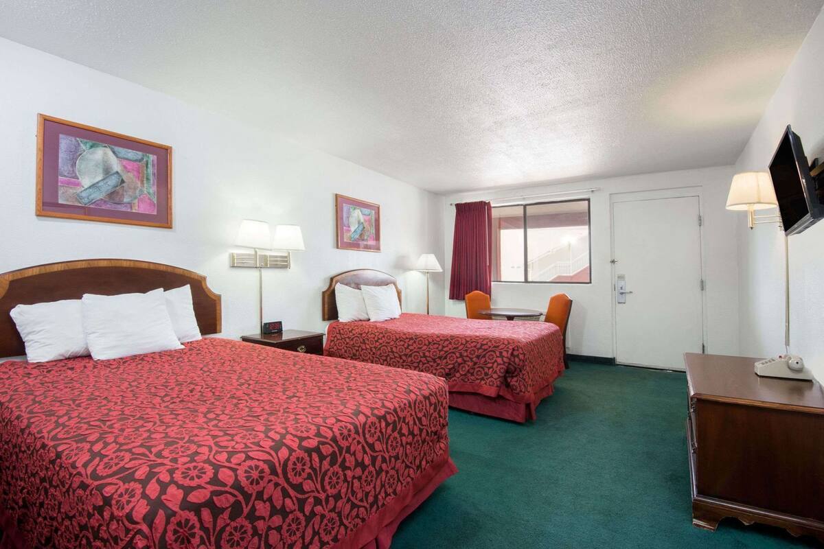 Habitación de hotel con dos camas, un escritorio, una silla, un televisor y obras de arte en las paredes.