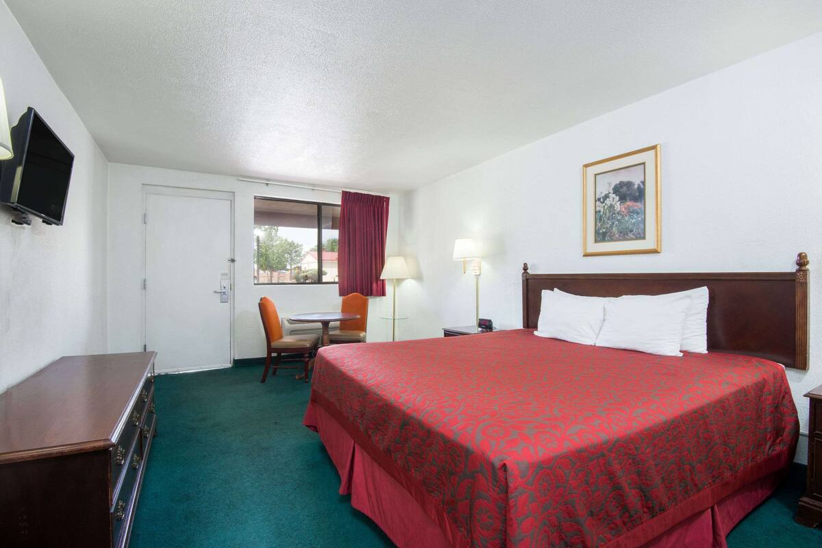 Habitación de hotel con una cama grande, un escritorio, una silla, un televisor y una ventana con cortinas.